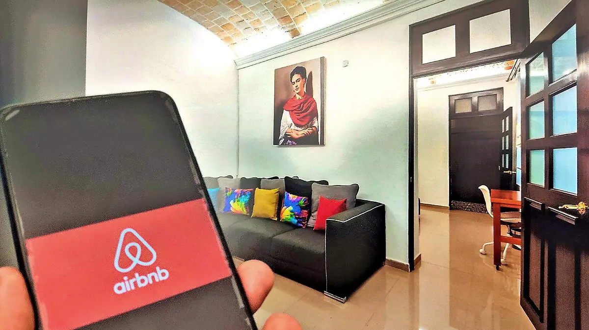 celular con imagen de airbnb frente a una computadora